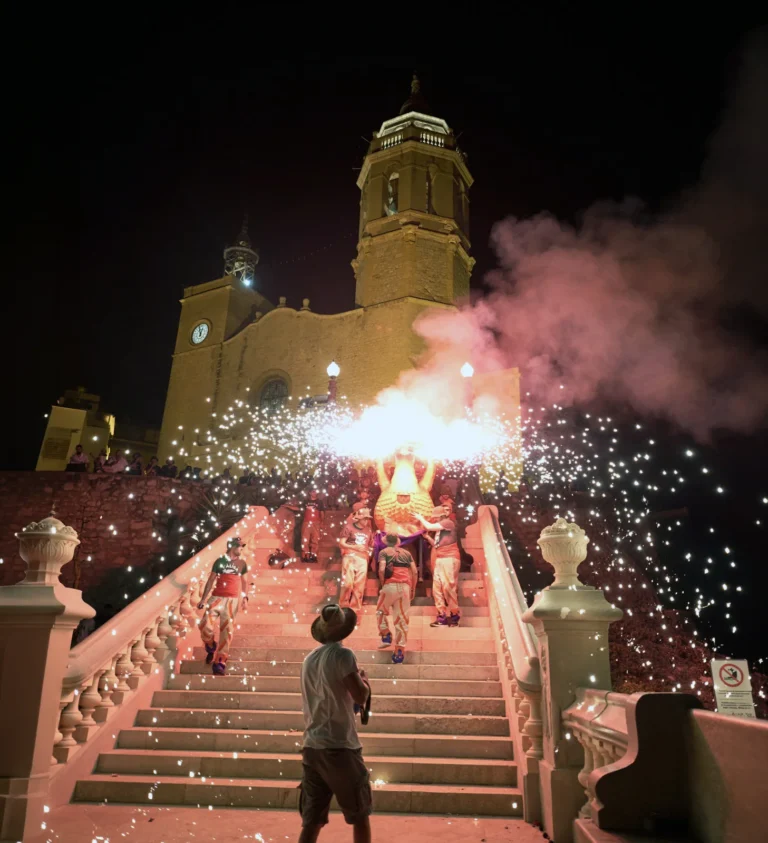 Fire groups and giants descend the steps of Sant Bartomeu church amid fire and smoke during the Baixada de les Escales celebration in Sitges.