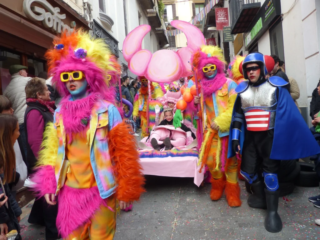Participantes con disfraces extravagantes y coloridos desfilan con una cama decorada durante la Carrera de Camas Disfrazadas del Carnaval de Sitges.