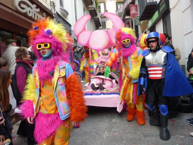 Participants in extravagant colourful costumes parading with a decorated bed during the Dressed-Up Bed Race at the Sitges Carnival.