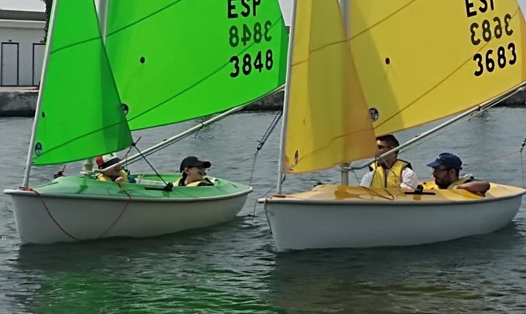 Two sailboats with young people sailing in calm waters during a school regatta in Sitges.