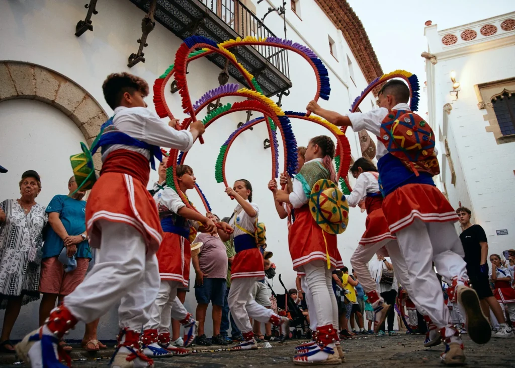 Niños de Sitges bailan la danza de las Cintas durante la Diada de Sant Tecla, con trajes tradicionales de colores en la plaza del pueblo.