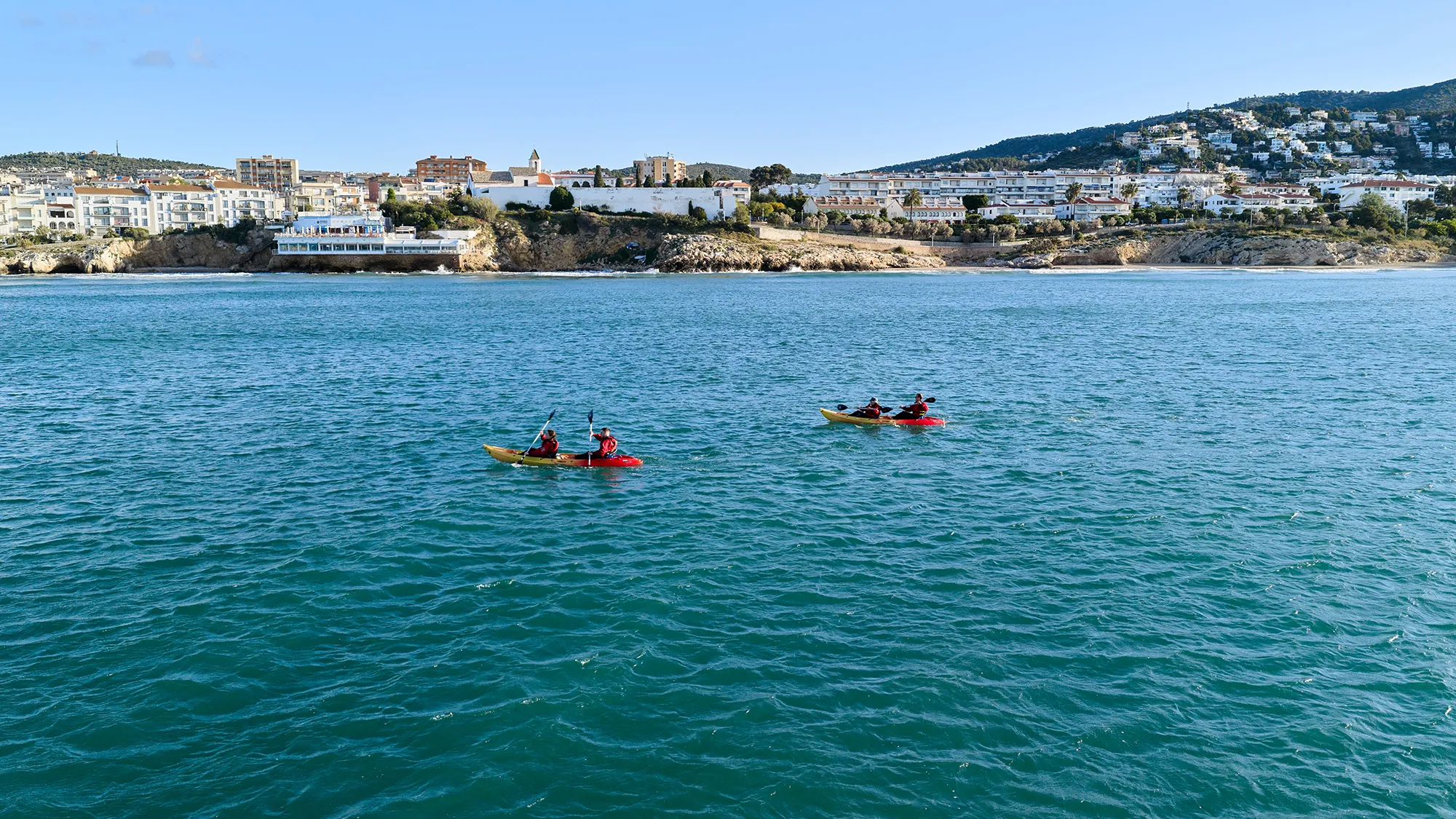 People kayaking between the coves of Sitges with the village in the background