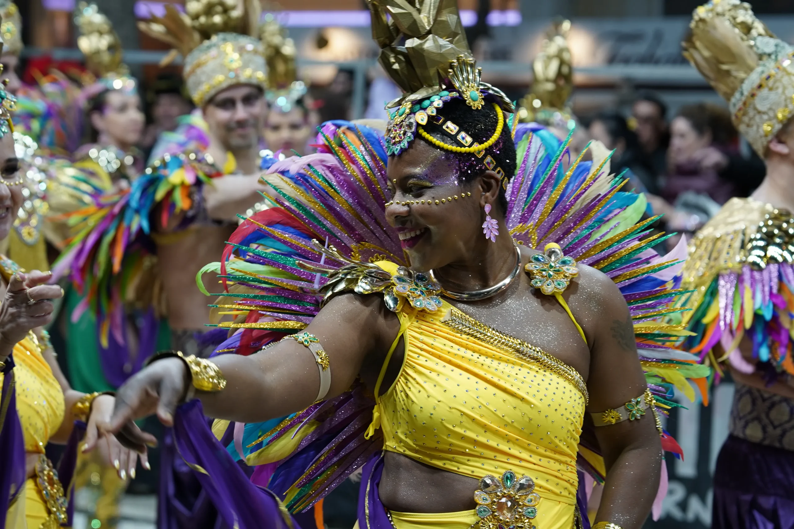 Bailarina con tocado de plumas multicolor y traje dorado y amarillo desfilando durante el Carnaval de Sitges.